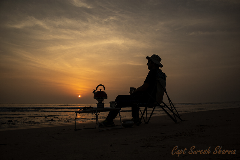 a guest enjoying morning tea and sunrise at our mobile glamping with caravan motorhome campervan in himachal for offbeat outdoor nomadic camp holiday for single woman girls to relax unwind at pong dam.