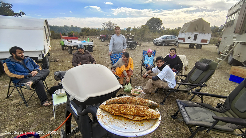 family of guests enjoying freshly cooked fish in a weber barbecue grill q3200 at offbeat location around pong dam in himachal pradesh with caravan in wilderness.